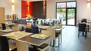 Un comedor moderno con varias mesas y sillas, una barra con alimentos y ventanas amplias que ofrecen vistas al exterior.