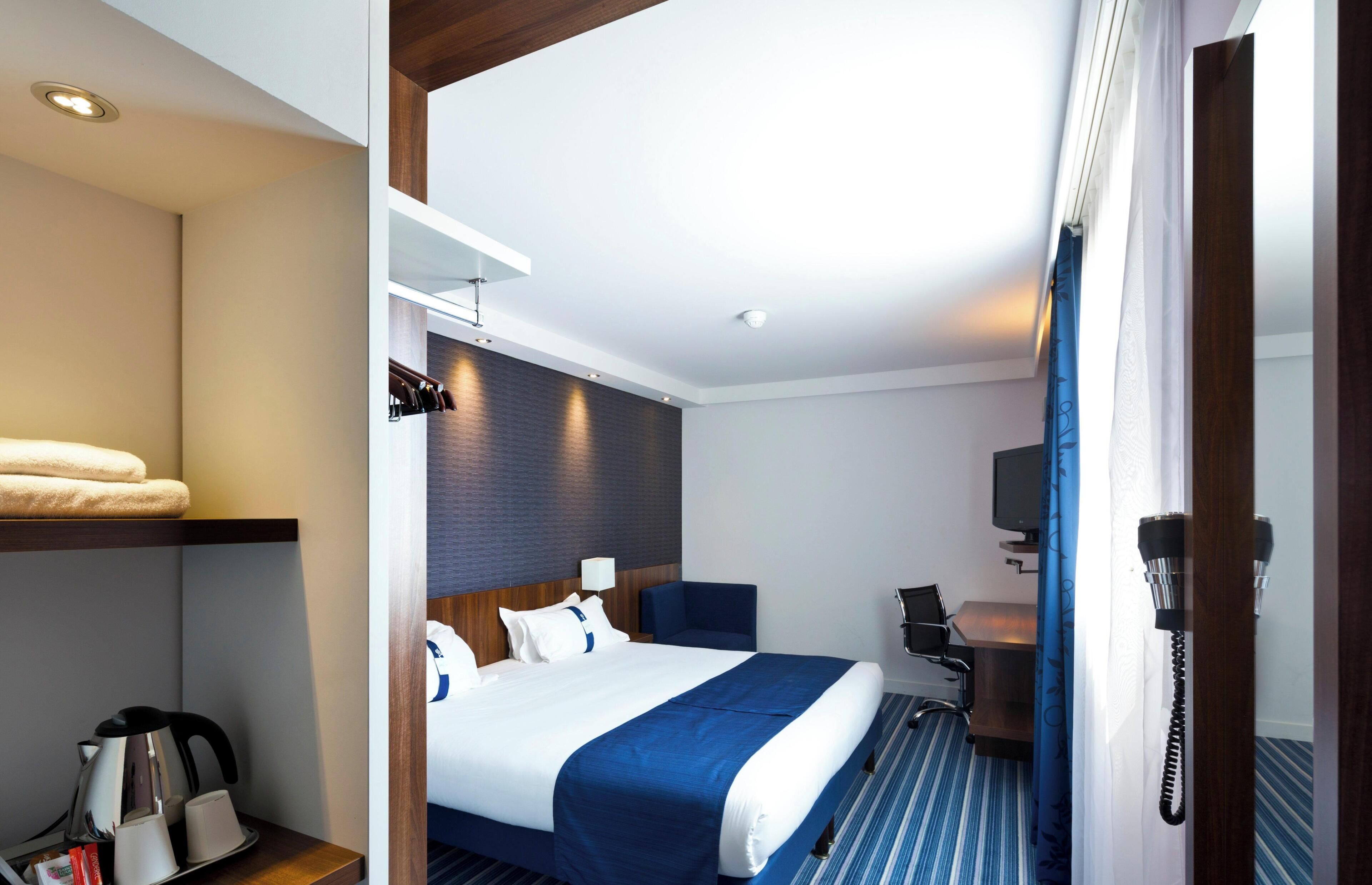 A hotel room with a bed, a desk, a chair, a telephone, and a television.