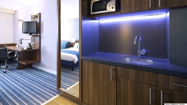 Una habitación de hotel moderna con un escritorio de madera, un televisor de pantalla plana, un microondas y un lavamanos.