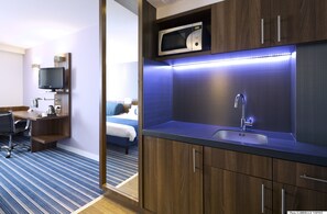 Una habitación de hotel moderna con un escritorio de madera, un televisor de pantalla plana, un microondas y un lavamanos.