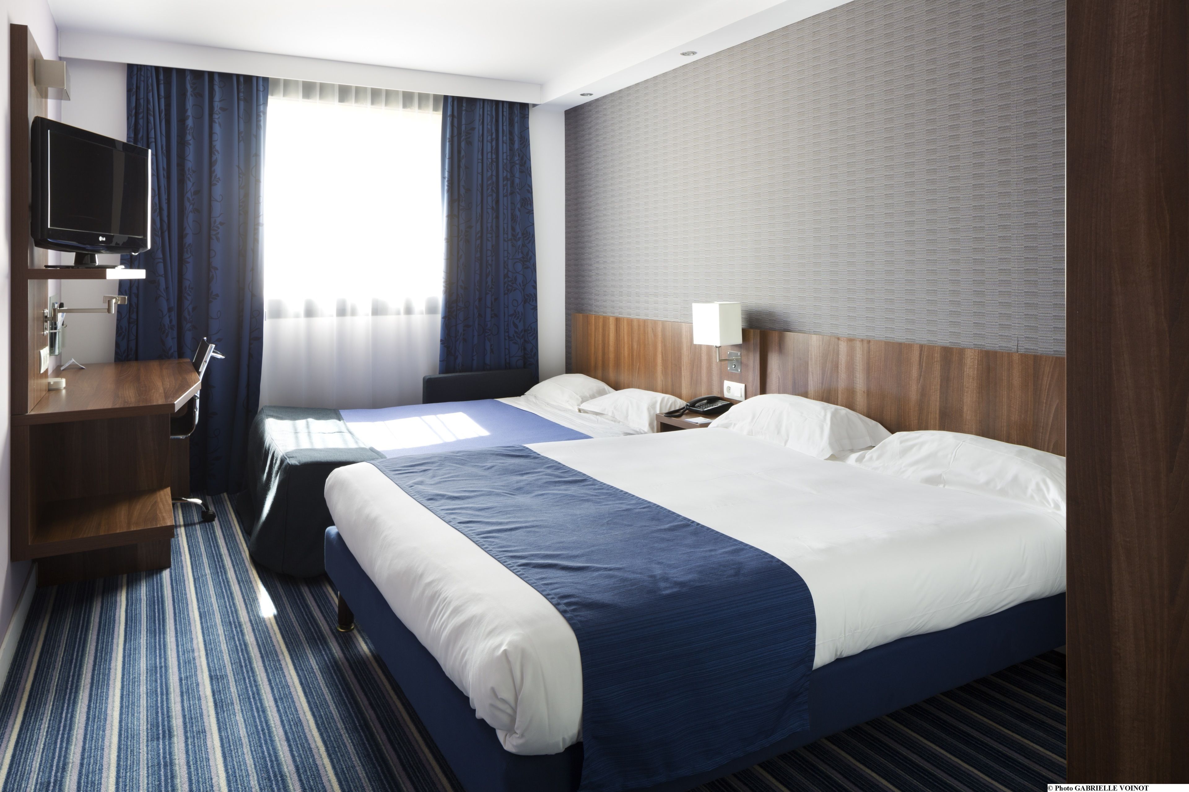 Ein Hotelzimmer mit einem großen Bett, einem Schreibtisch, einem Fernseher und einem Fenster mit Vorhängen.