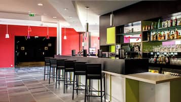 A modern bar area with a counter, stools, and a variety of bottles and glasses.