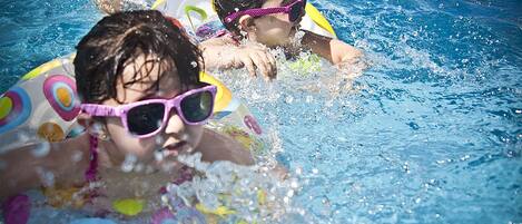 Two individuals in a swimming pool with inflatable rings.
