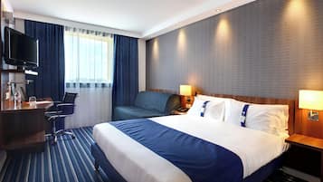 Habitación de hotel con cama, escritorio, silla, televisión y ventana con cortinas.