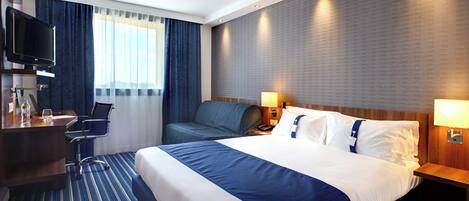 A hotel room with a bed, a desk, a chair, a television, and a window with curtains.