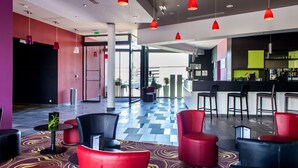 Un hall de hotel con sillas rojas y negras, una recepción y una zona de bar.