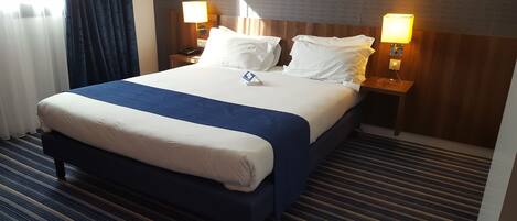 Una habitación de hotel con una cama grande, dos lámparas de noche, un cabecero de madera y una alfombra a rayas.