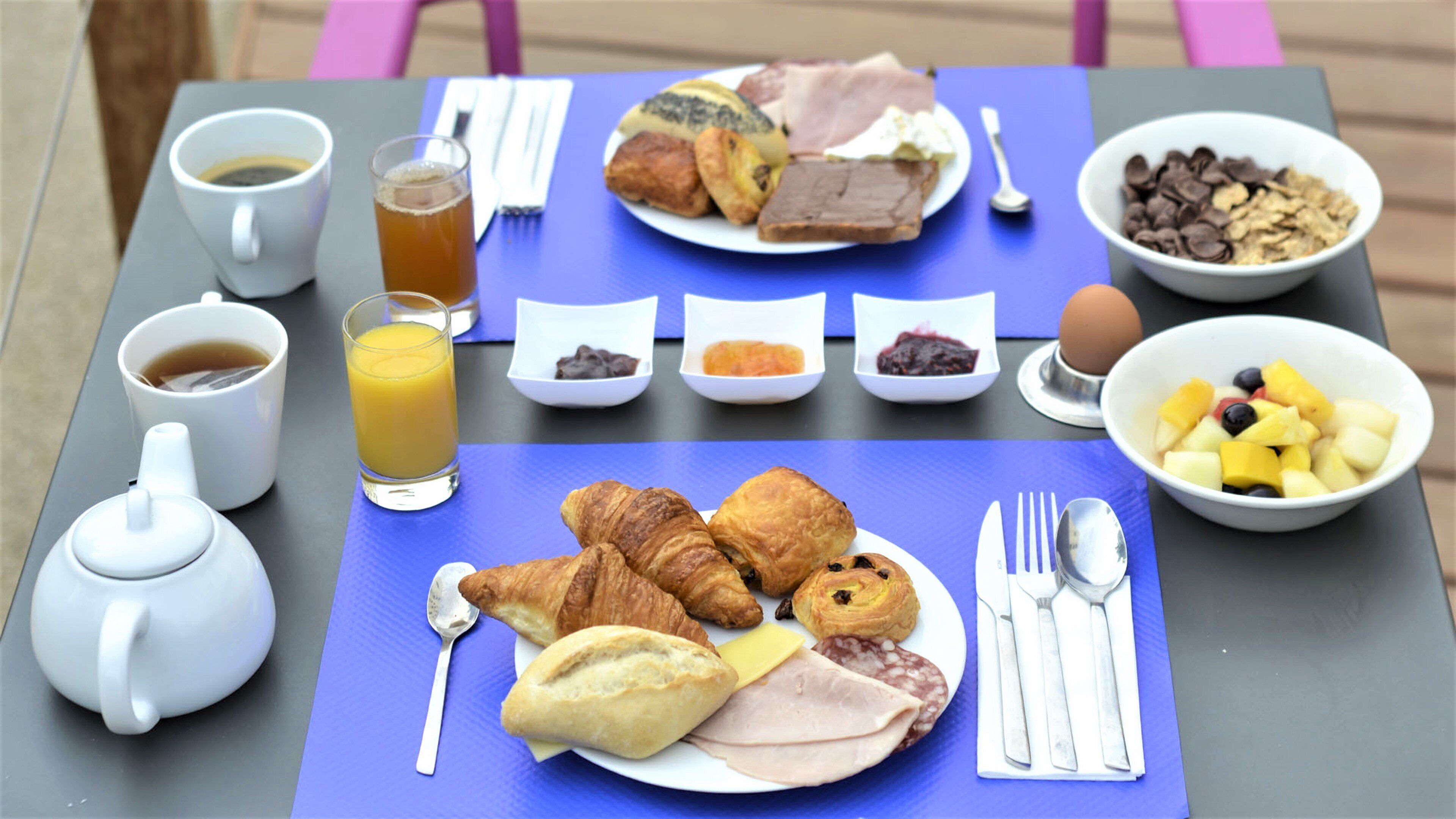 Ein Frühstückstisch mit verschiedenen Speisen, einer Kaffeetasse, einem Glas Orangensaft und einer Teekanne.