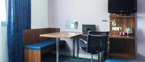 A hotel room with a desk, chair, bench, television, and a small shelf with items.