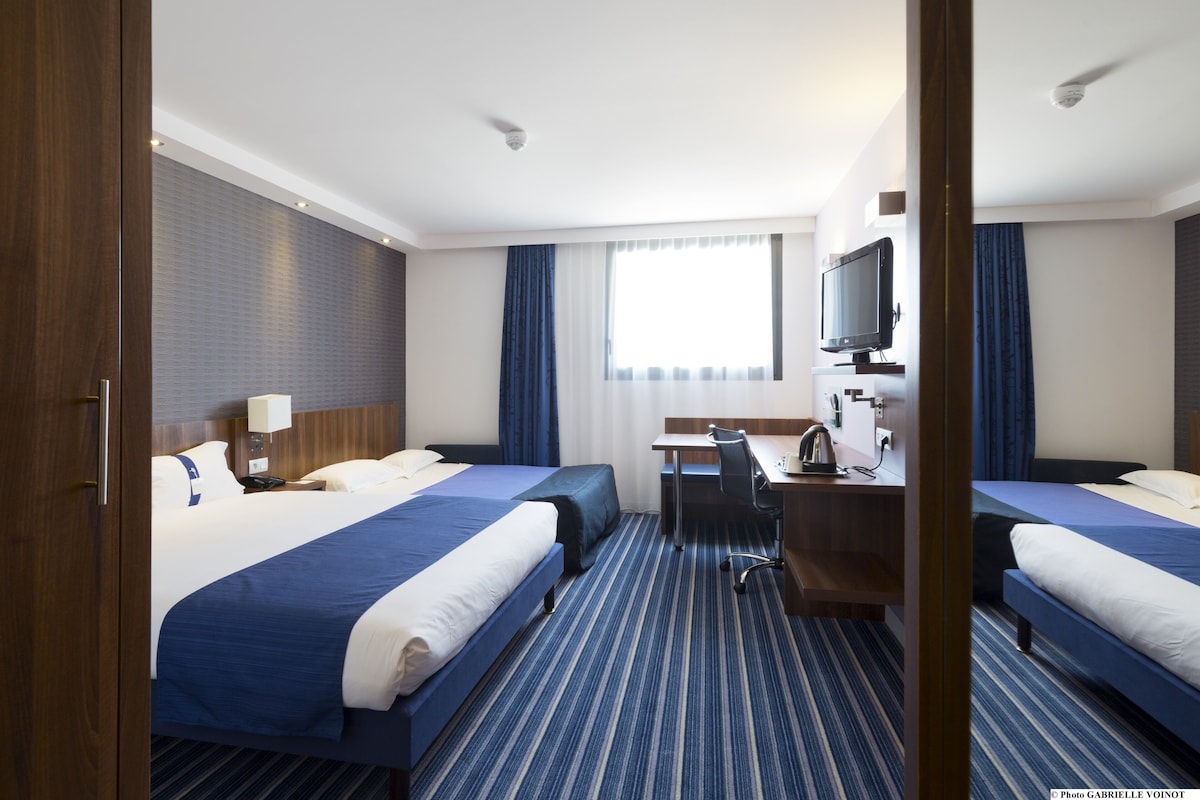 A hotel room with two beds, a desk, a chair, a TV, and a window with curtains.
