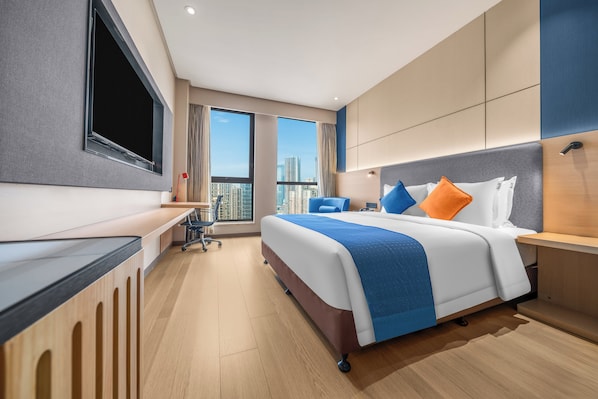 Quarto de hotel moderno com uma cama grande, uma escrivaninha e uma televisão.