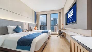 A modern hotel room with two beds, a desk, and a large window offering a city view.