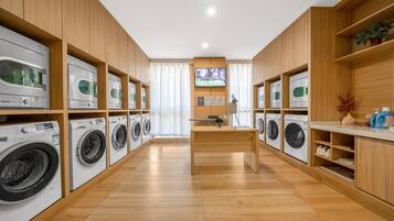 A laundry facility with multiple washing machines, wooden cabinets, and a central table.