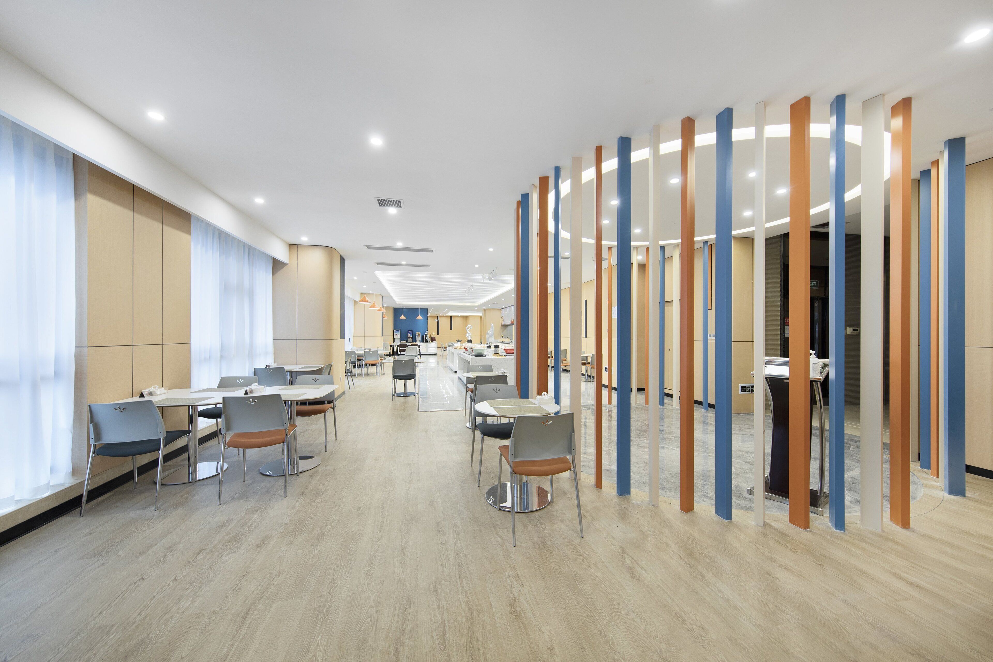 Un espace repas moderne avec des tables et des chaises rondes, un parquet en bois clair et une vue sur la cuisine en arrière-plan.