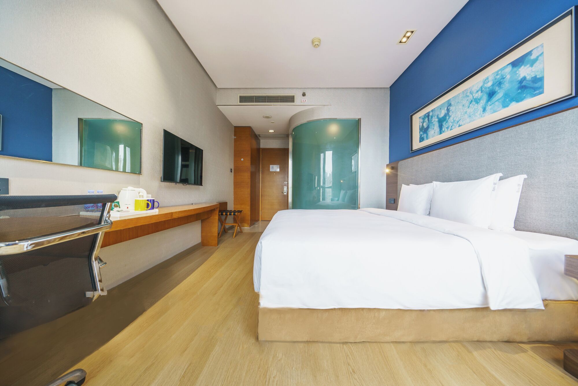 A hotel room with a bed, a desk with a chair, a television, and a large window.