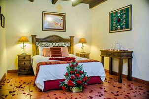 Una cama bien hecha con una colcha blanca y roja, dos lámparas de noche, un cabecero de madera y una mesita con un objeto decorativo.