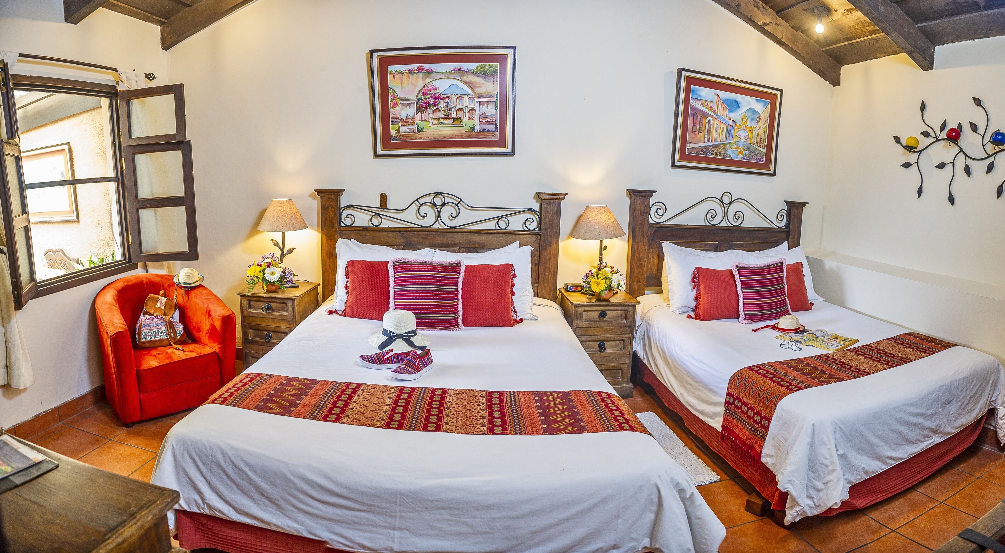 Habitación de hotel con dos camas, un sillón rojo y obras de arte en las paredes.