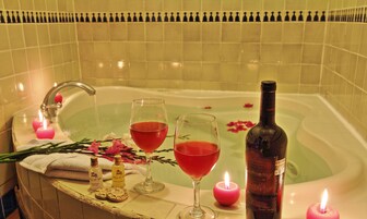 Una bañera con dos vasos de líquido rojo, una botella de vino y velas.