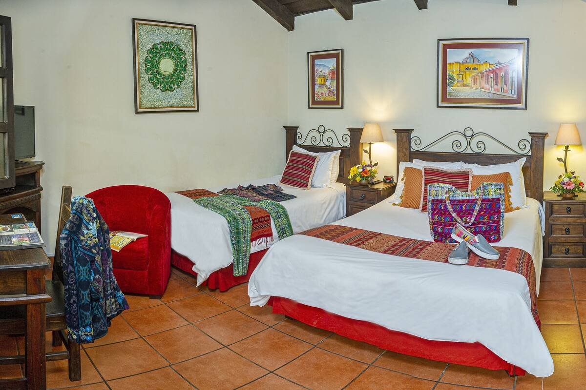 Un dormitorio con dos camas, un escritorio y una silla. Hay cuadros en las paredes y una ventana con cortinas.