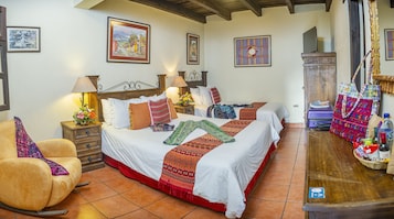 Una habitación de hotel con una cama grande, dos mesitas de noche, una silla y un aparador de madera.