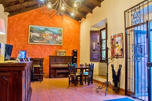 A cozy room with a piano, wooden chairs, a table with a vase, and a painting on the wall.