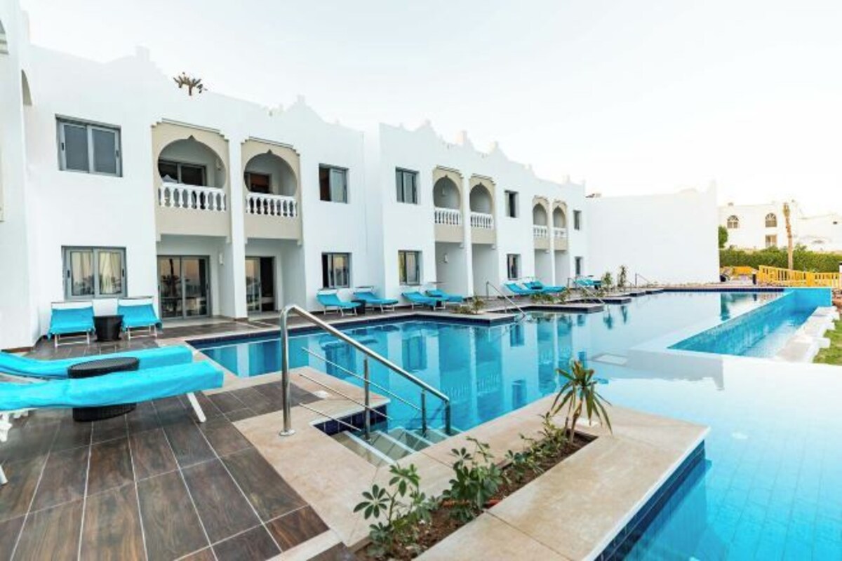 A hotel with a swimming pool, outdoor seating, and a white facade.