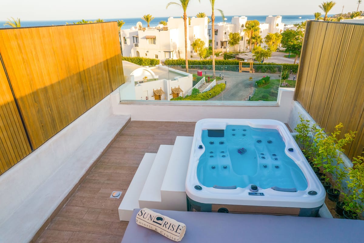 Eine Dachterrasse mit Whirlpool, einem Schild mit der Aufschrift "Sunrise Resorts & Cruises" und Blick auf das Meer und Gebäude im Hintergrund.