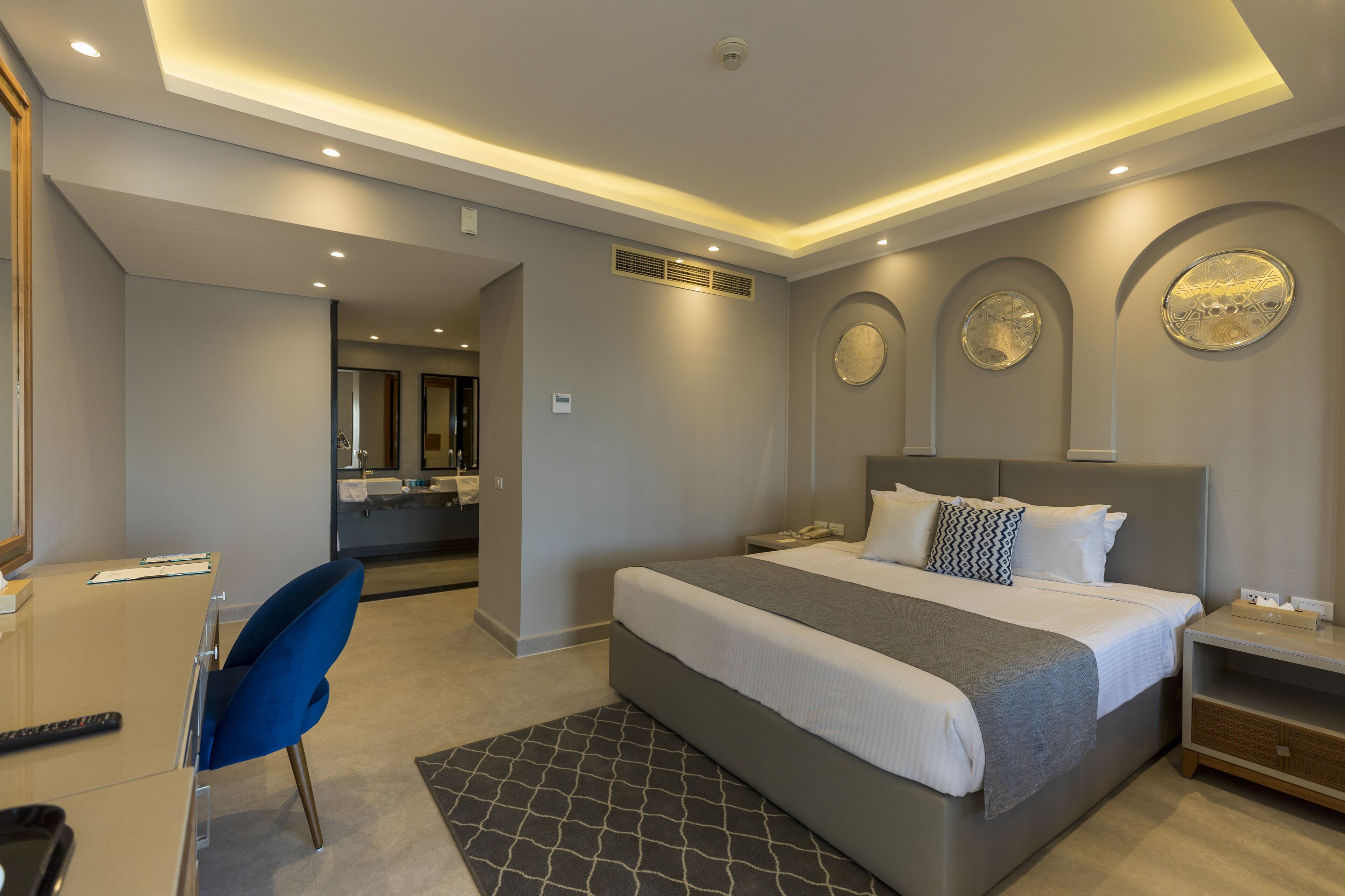 Une chambre d’hôtel moderne avec un grand lit, un bureau, une chaise et une salle de bain visible au fond.