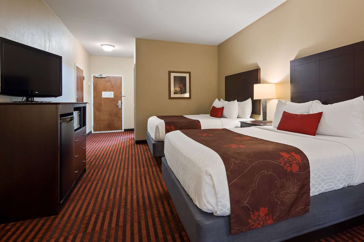 Quarto de hotel com duas camas, televisão, escrivaninha e porta.