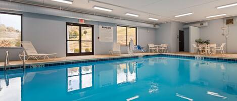 Une piscine à l’eau claire, un poste de surveillance pour le sauveteur, des chaises longues et un panneau indiquant les règles.