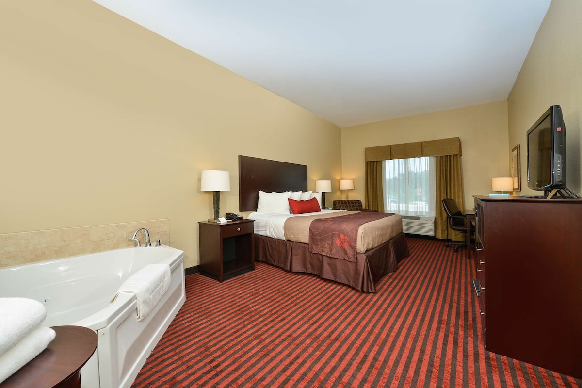 Quarto de hotel com uma cama grande, banheiro separado com banheira, escrivaninha e televisão.