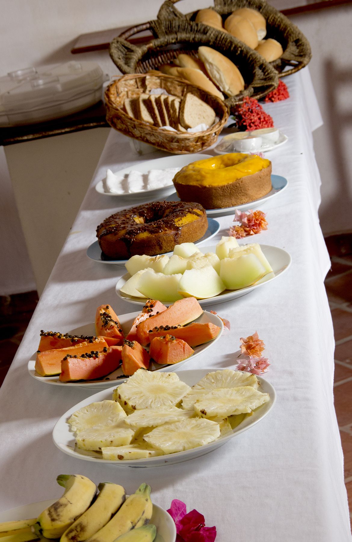 Une table de buffet proposant une variété d’aliments, notamment du pain, des gâteaux, des fruits et des légumes.