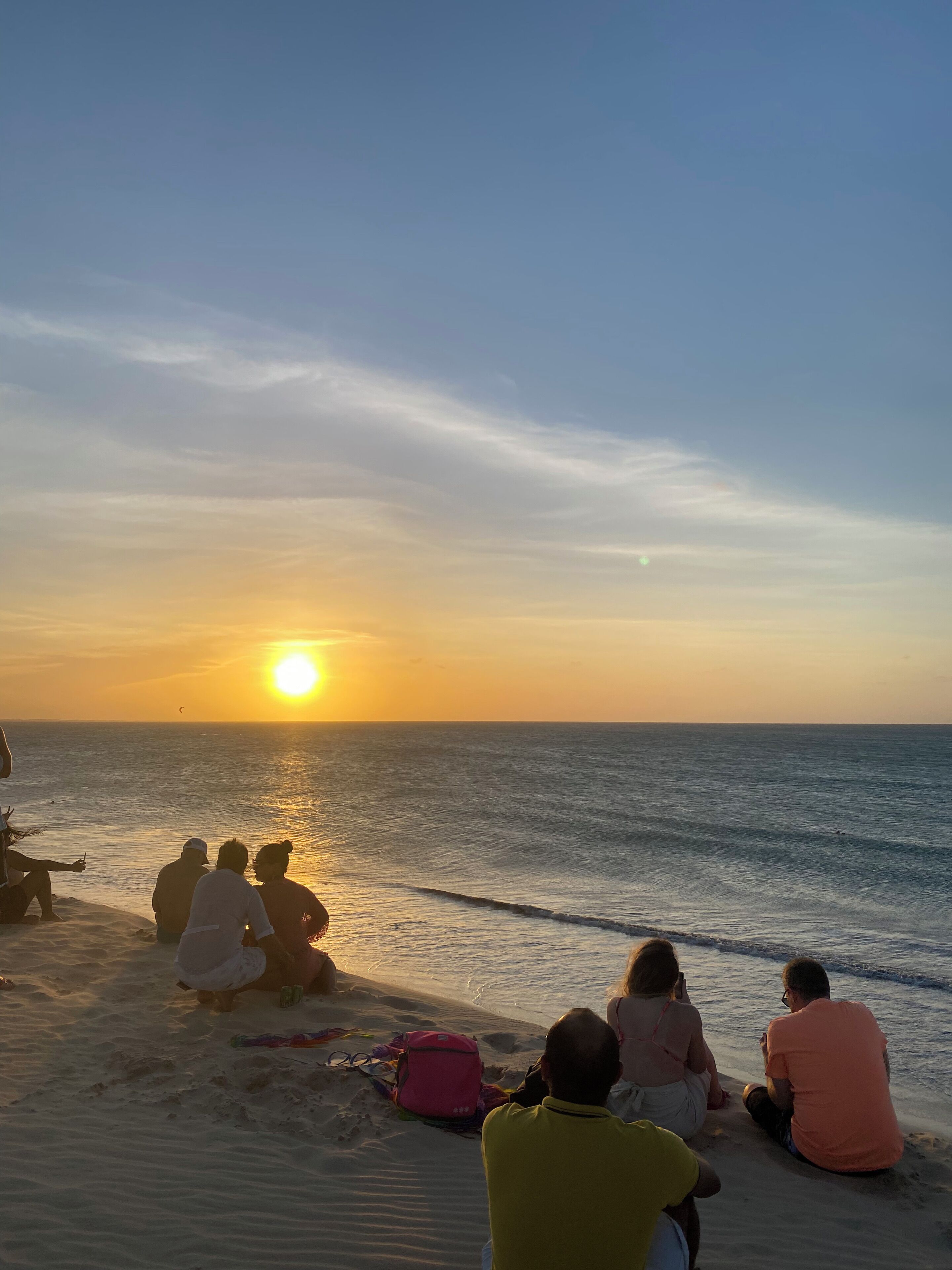 Ein Sonnenuntergang am Strand, Menschen sitzen im Sand.