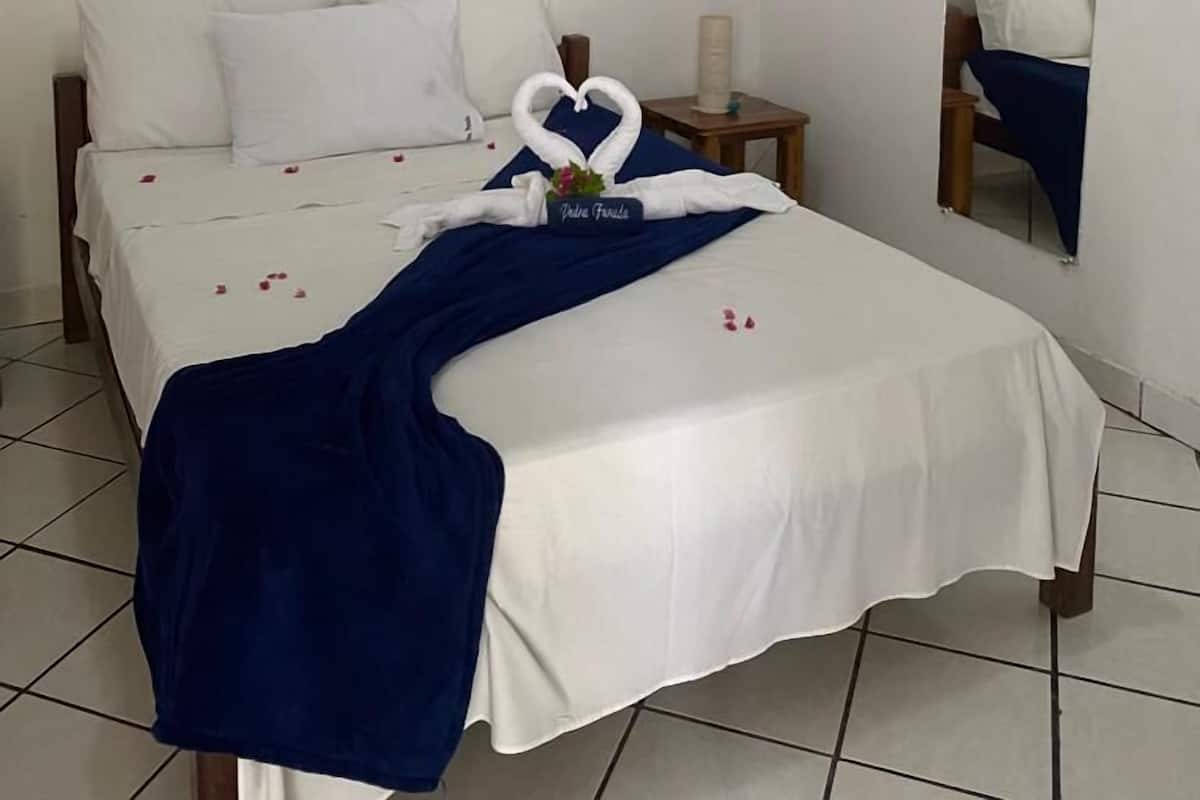 Ein ordentlich bezogenes Bett mit weißen Leinen, einer blauen Decke und einer Herz-förmigen Handtuchdeko.