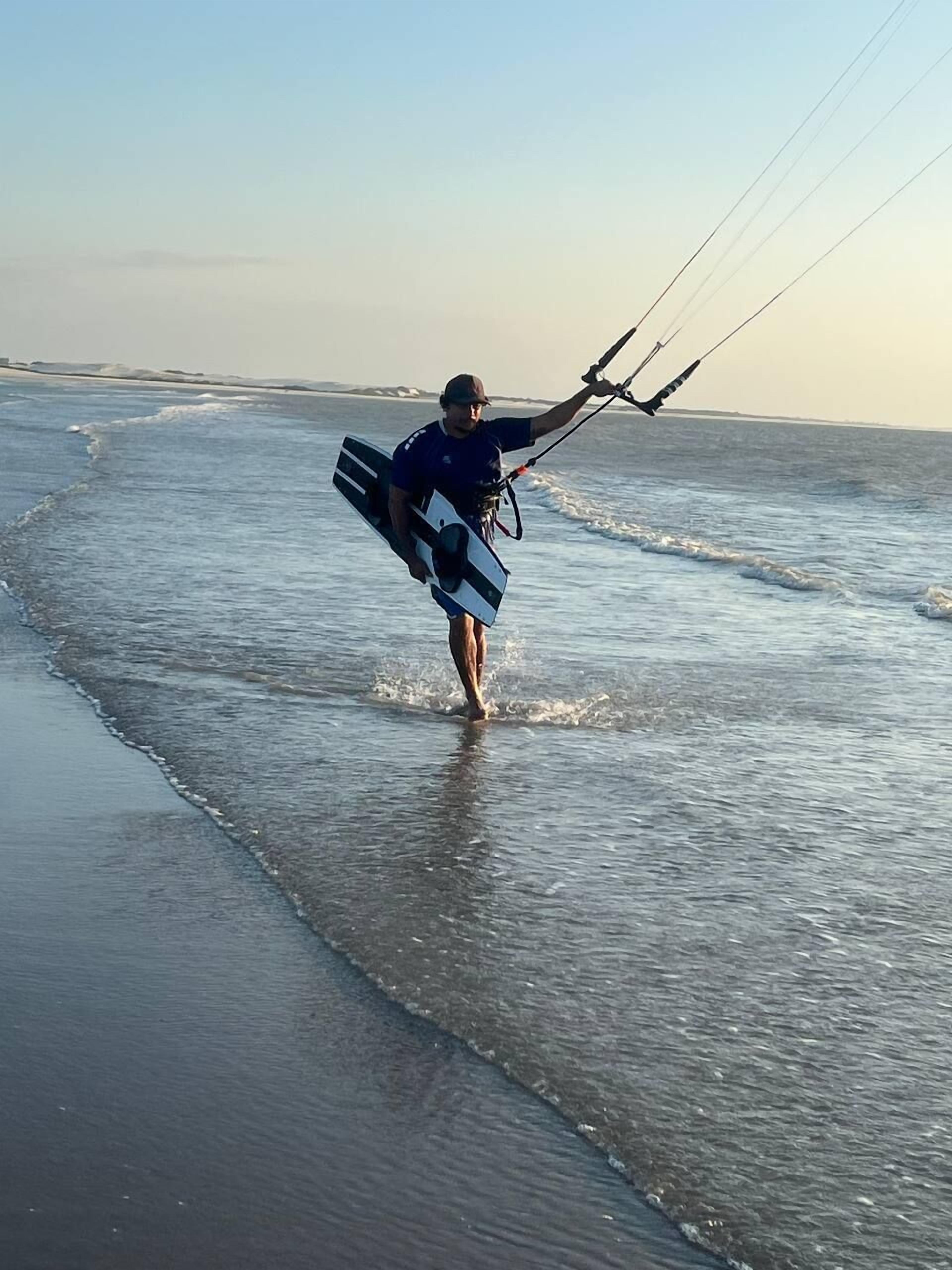 A person walking on a beach with a kiteboard.