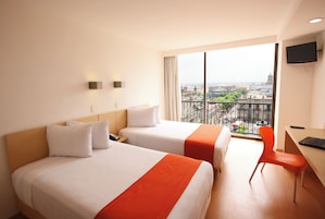 A hotel room with two beds, a desk, a chair, and a TV.