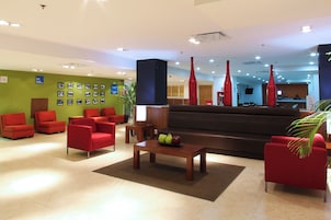 A modern lobby with red chairs, a black sofa, and a coffee table with fruit.