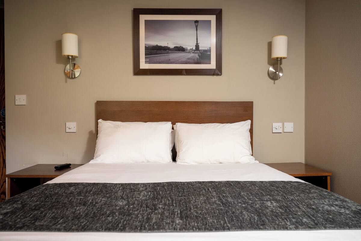 A hotel room with a large bed, two bedside tables, a framed picture on the wall, and two wall-mounted lamps.