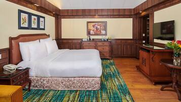 A hotel room with a large bed, wooden furniture, a desk with a TV, and framed artwork on the walls.