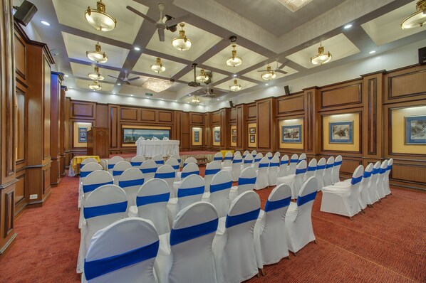 A large conference room with rows of white chairs with blue sashes, wooden paneling, and ceiling fans.