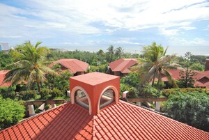 A red-tiled roof with a central skylight, surrounded by lush greenery and palm trees.