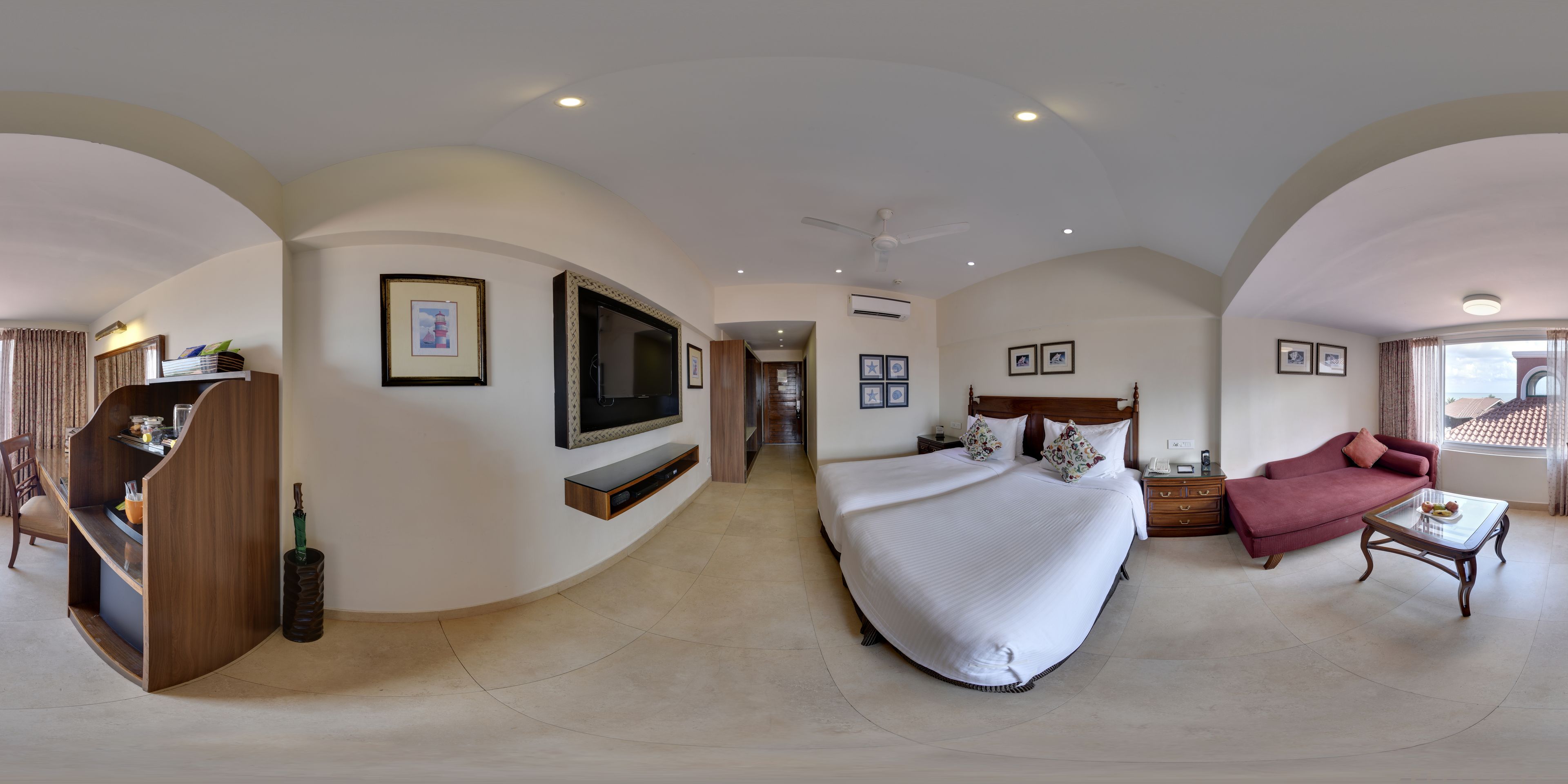 Quarto espaçoso com cama grande, TV na parede, área de estar com sofá e poltrona, e mesa de jantar.