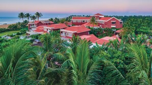 A coastal resort with multiple red-roofed buildings, lush greenery, and a view of the ocean. - MAYFAIR Heritage, Puri (Puri)