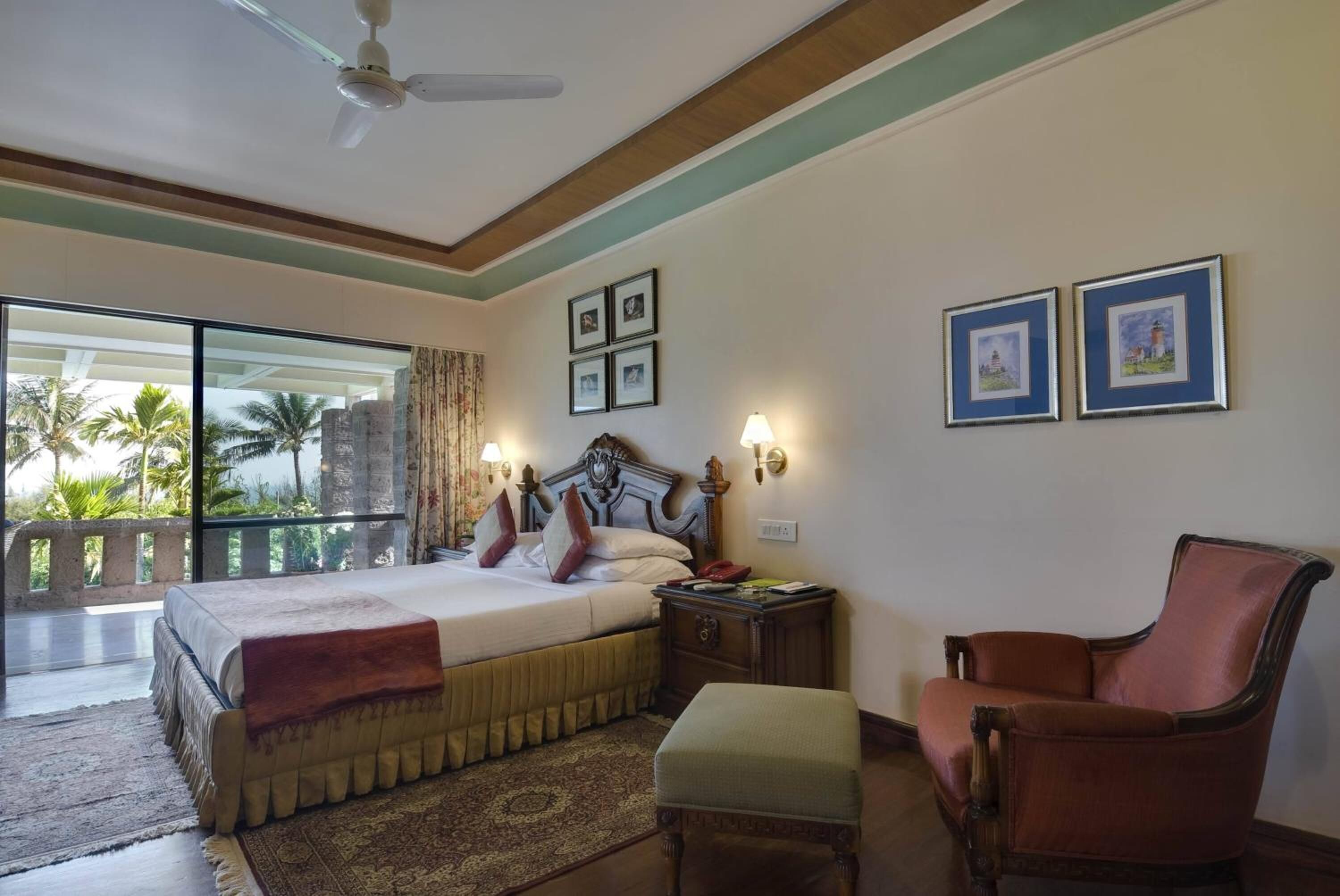A hotel room with a bed, a chair, a nightstand, and a view of palm trees and buildings.