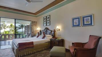 A hotel room with a bed, a chair, a nightstand, and a view of palm trees and buildings.
