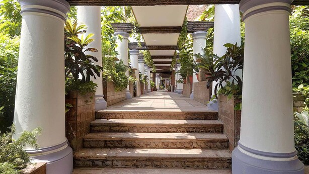 A covered walkway with stone steps and white columns, surrounded by greenery. - MAYFAIR Heritage, Puri (Puri)