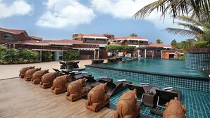 A pool area with elephant-shaped lounge chairs, a pool with blue tiles, and a building with red-tiled roofs in the background. - MAYFAIR Heritage, Puri (Puri)
