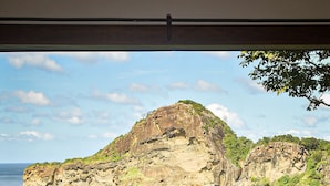 A wooden deck with two rocking chairs and a small table, overlooking a coastal landscape with cliffs and the sea. - Aqua Oceanfront Hotel Resort (Tola)