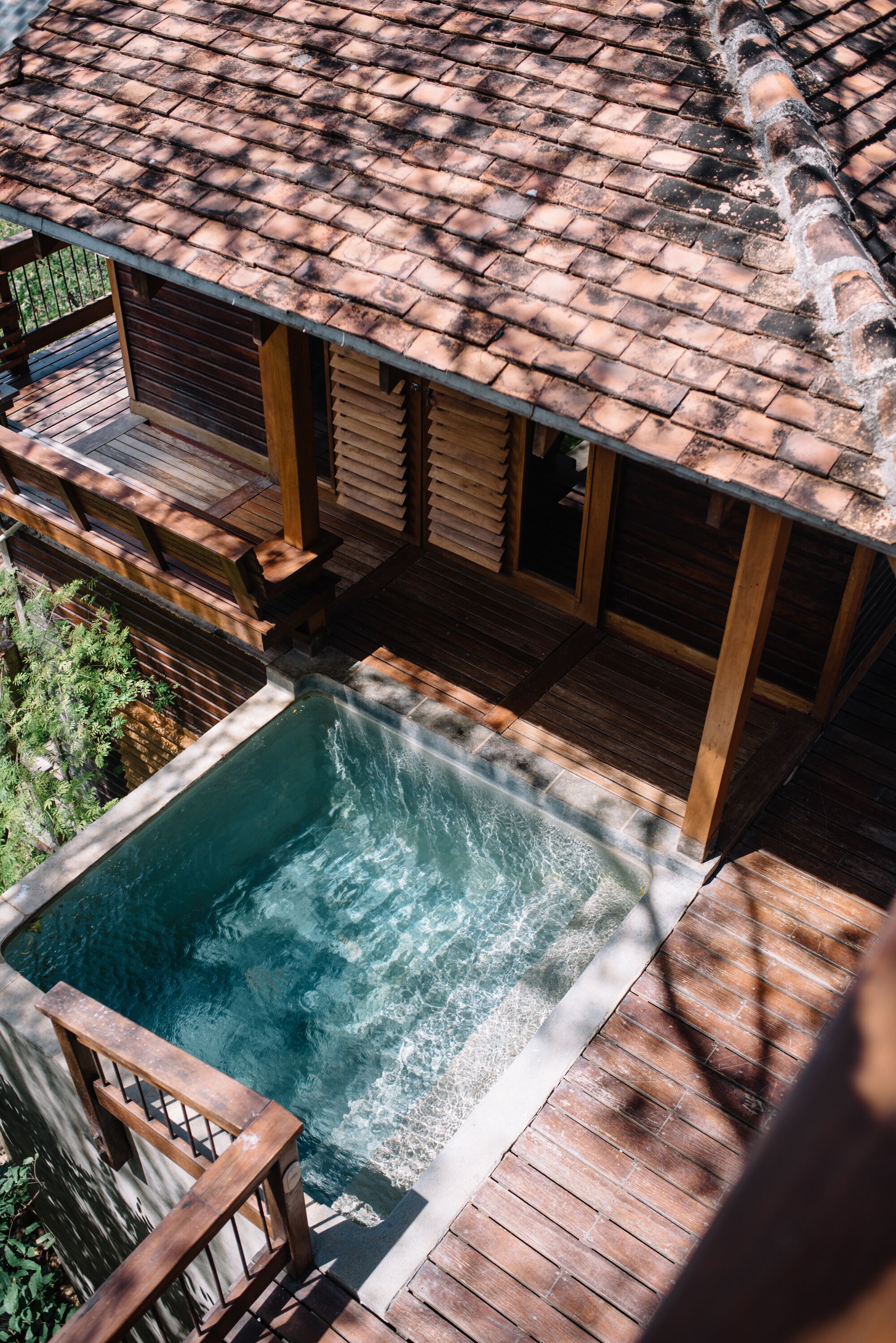 Una terraza de madera con un jacuzzi y una piscina, rodeada por un cerco de madera y follaje.
