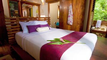 Una cama bien hecha con una colcha blanca y granate, un cabecero de madera y un banco de madera al pie de la cama.